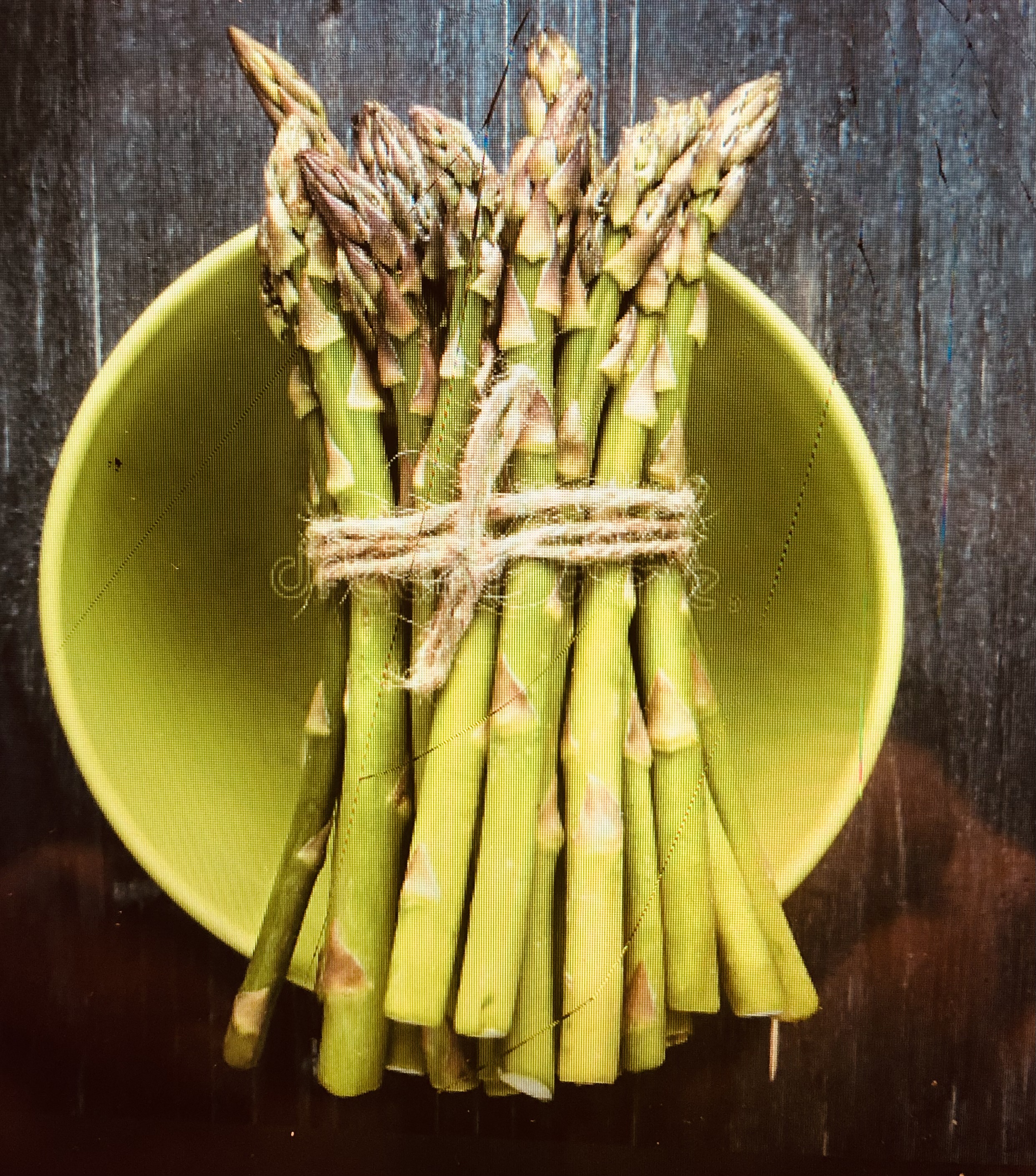 A color photo of a bundle of asparagus tied with twine and sitting atop a green bowl.