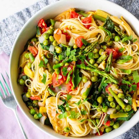 A photo of a white bowl filled with angel hair pasta and vegetables.