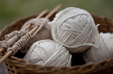 A color photo of balls of yarn and knitting needles in a basket.