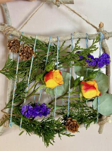 A photo of a botanical frame make with sticks, leaves and flowers.