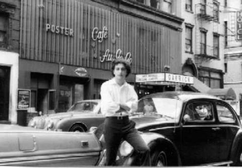 A black and white photo of a man sitting on a car in front of Cafe Au Go Go.