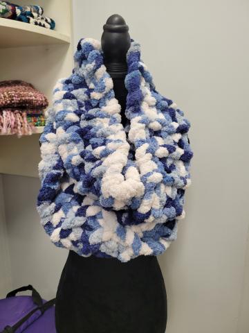 A color photo of a chunky hand-knit scarf hanging on a dress form.
