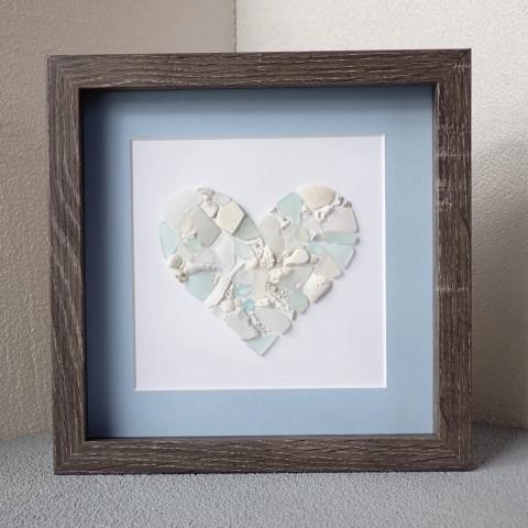 A photo of a seaglass heart framed in brown with a light blue matte.