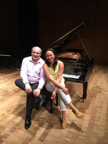 A color photo of Pablo Lavandera and Evelyn Ulex seated on a piano bench next to a grand piano. 