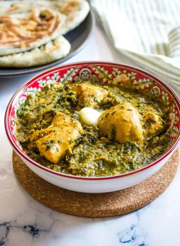 A photo of a bowl of Spinach Chicken accompanied by a side of flatbread.