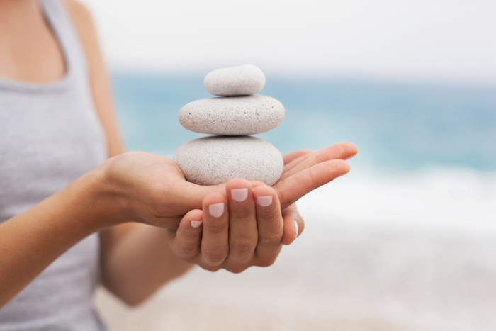 Photo of a woman's hands holding three white stones stacked atop one another.