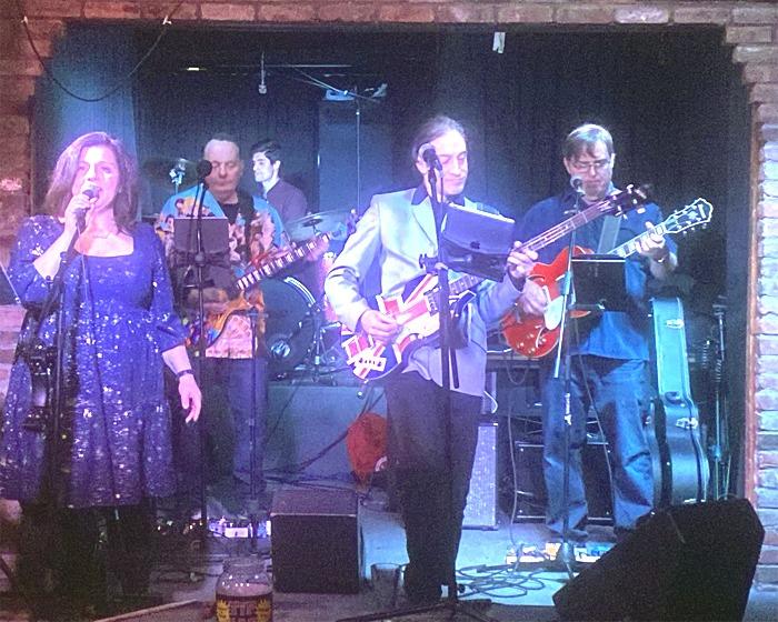 A photo of members of The Day Trippers Band singing and playing instruments.