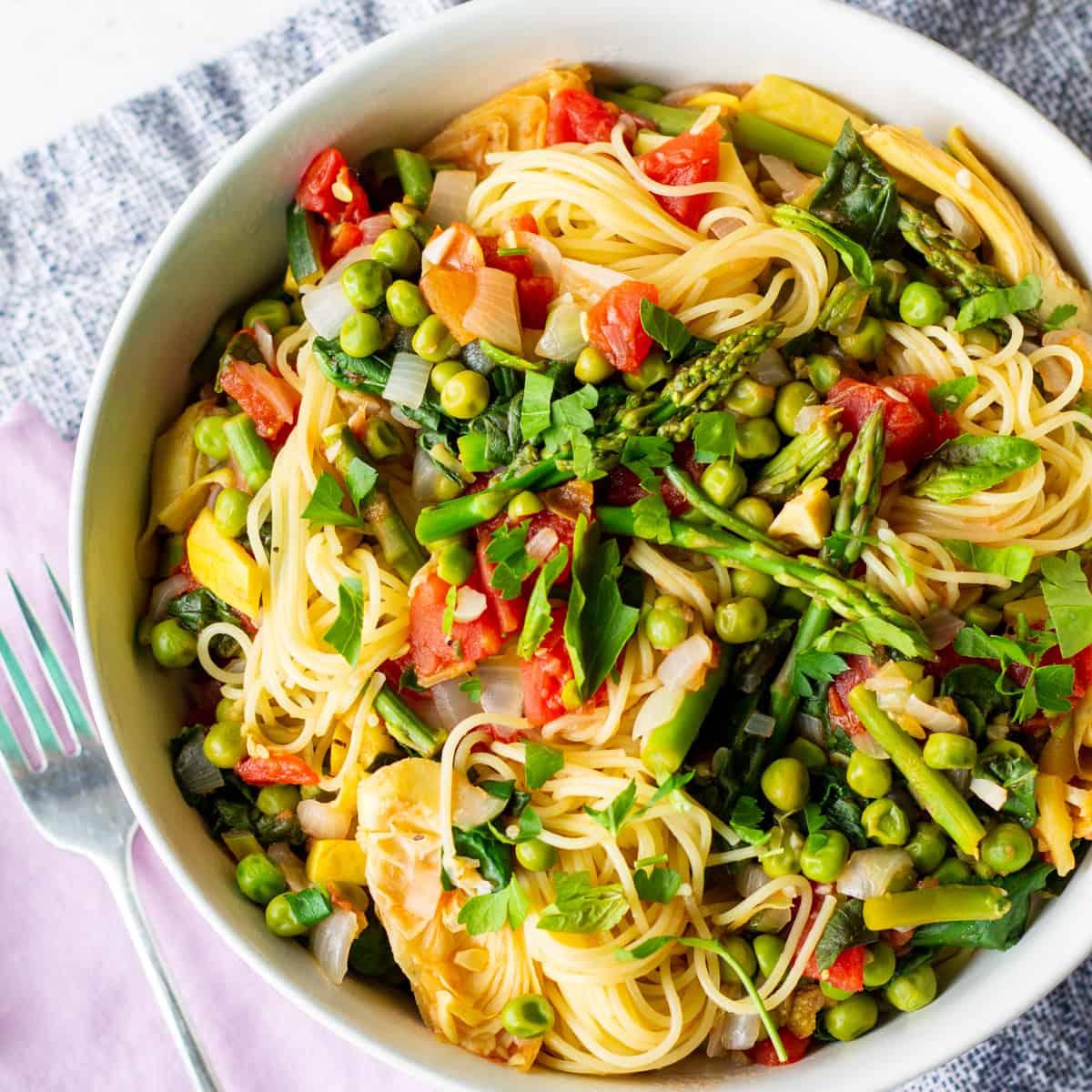 A photo of a white bowl filled with angel hair pasta and vegetables.