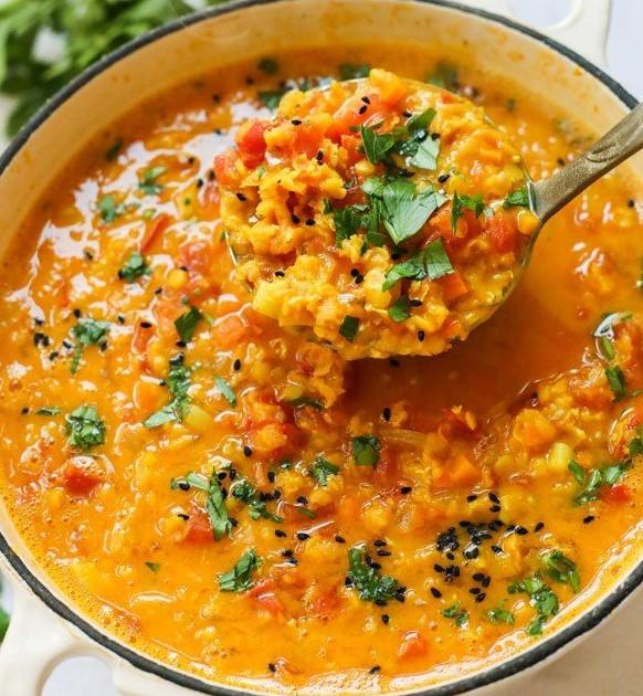 A photo of a pot of lentil soup, with a portion being scooped out with a ladle.