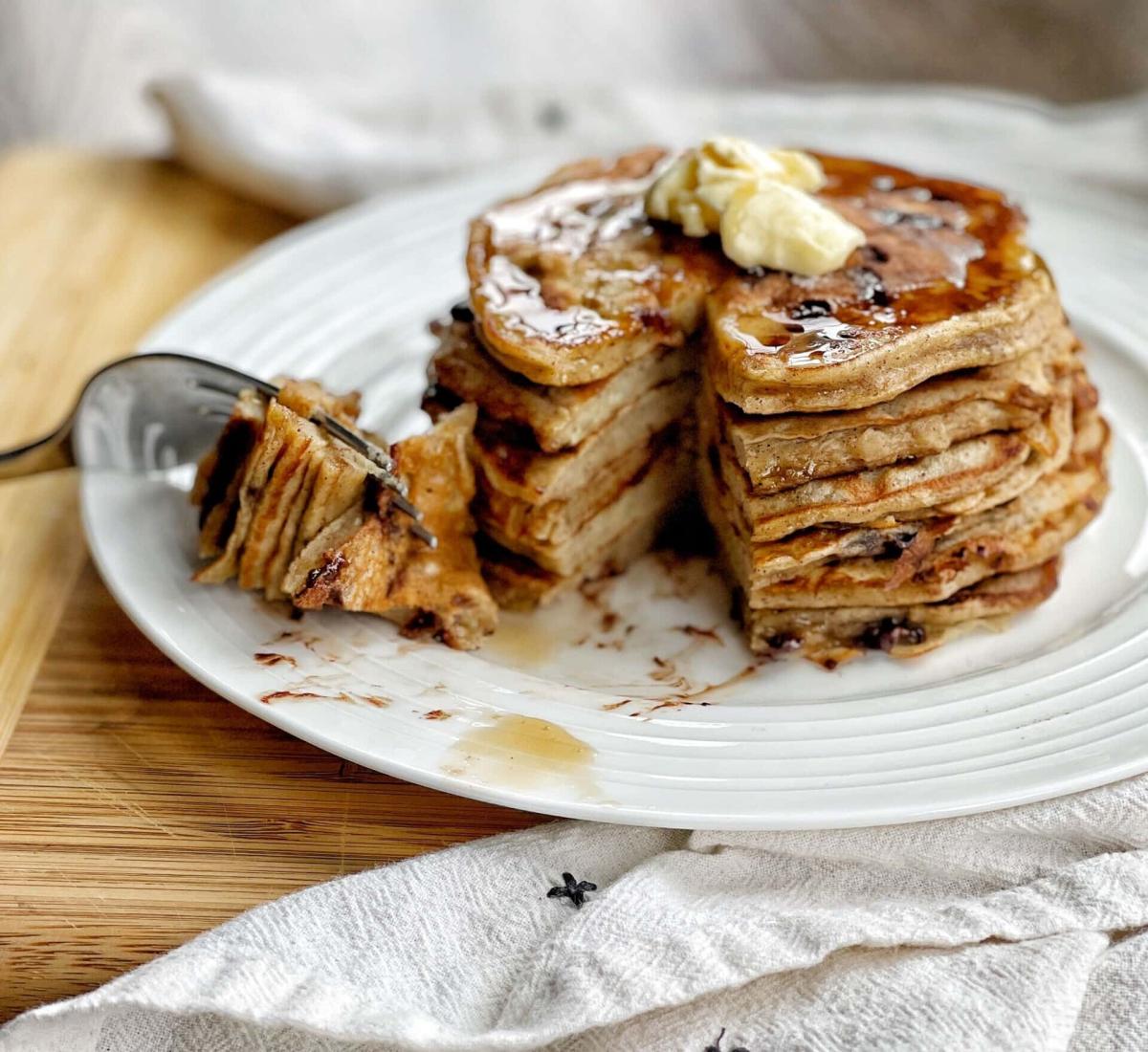 A color photo of a stack of pancakes on a white plate with a portion on a fork.