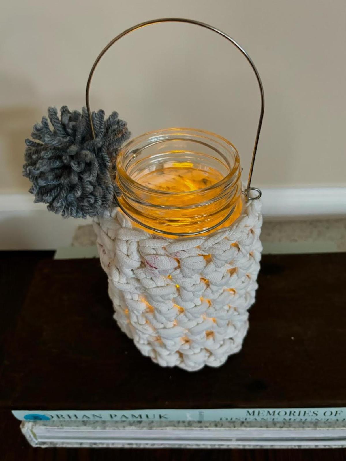 A photo of a mason jar candle holder enrobed in a crocheted wrapper. 