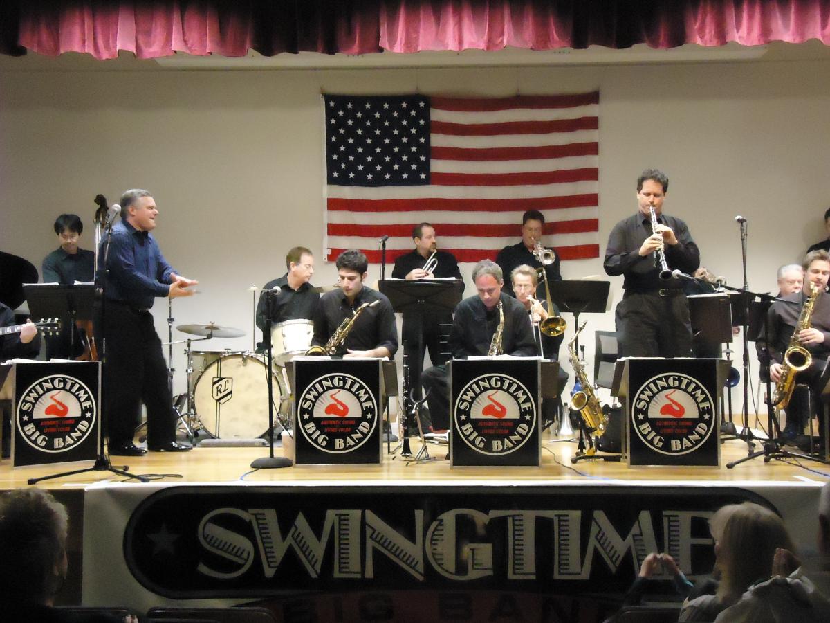Members of the Swingtime Big Band on stage with an American flag in the background.