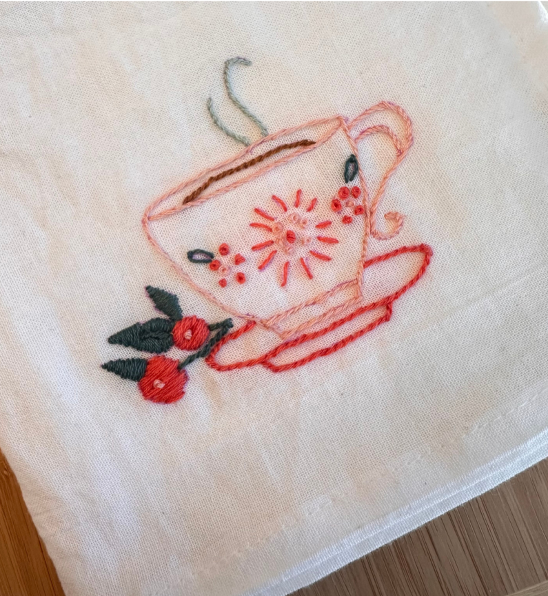 A photo of an embroidered tea towel featuring a teacup and flowers.
