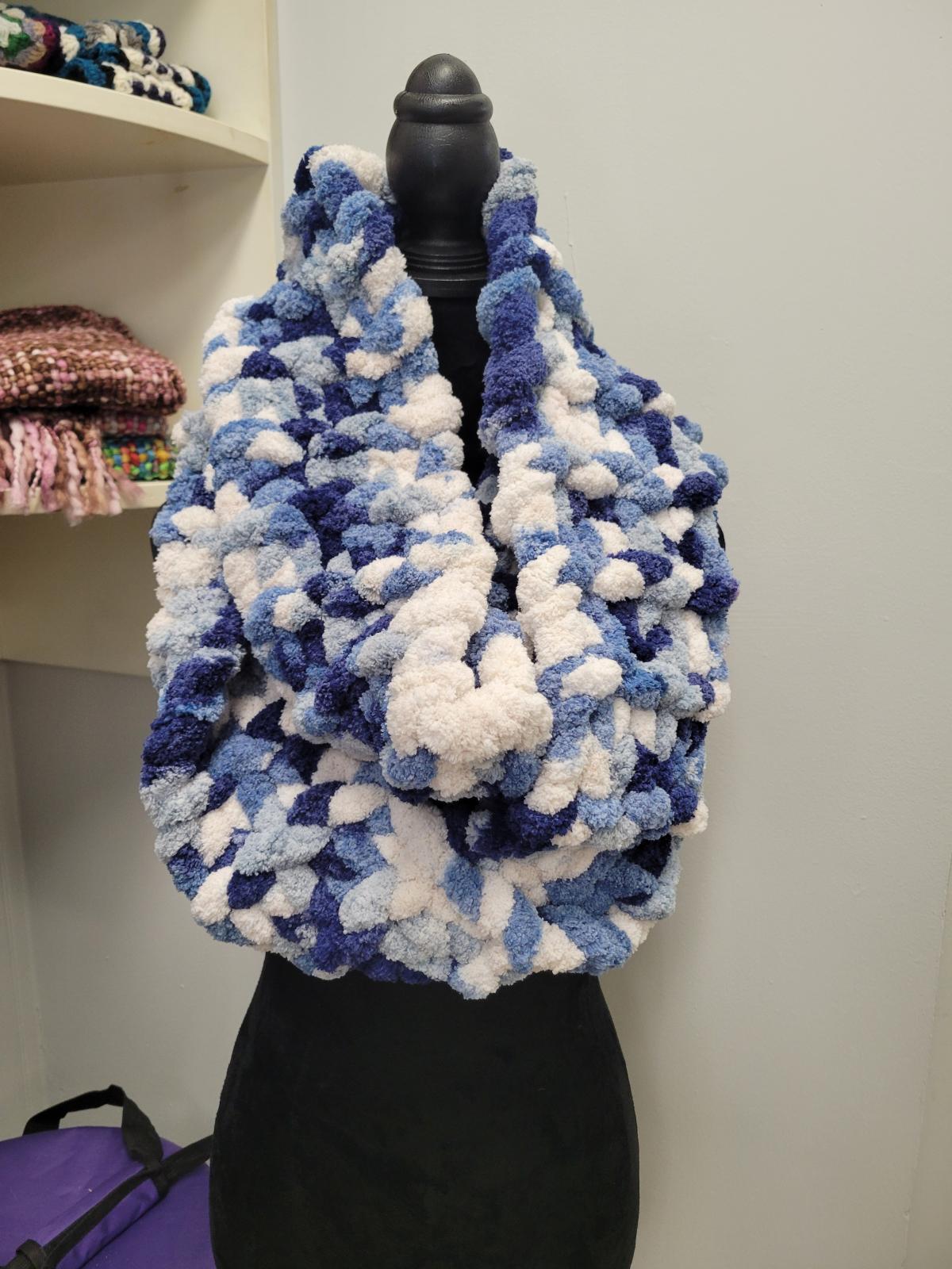 A color photo of a chunky hand-knit scarf hanging on a dress form.
