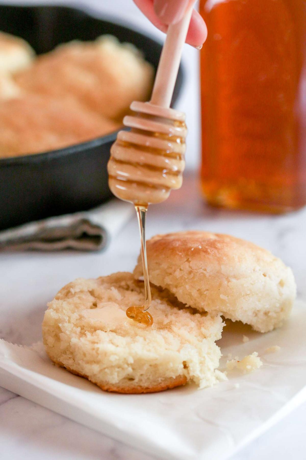 A photo of a wooden honey dipper drizzling honey on top of a cut biscuit.