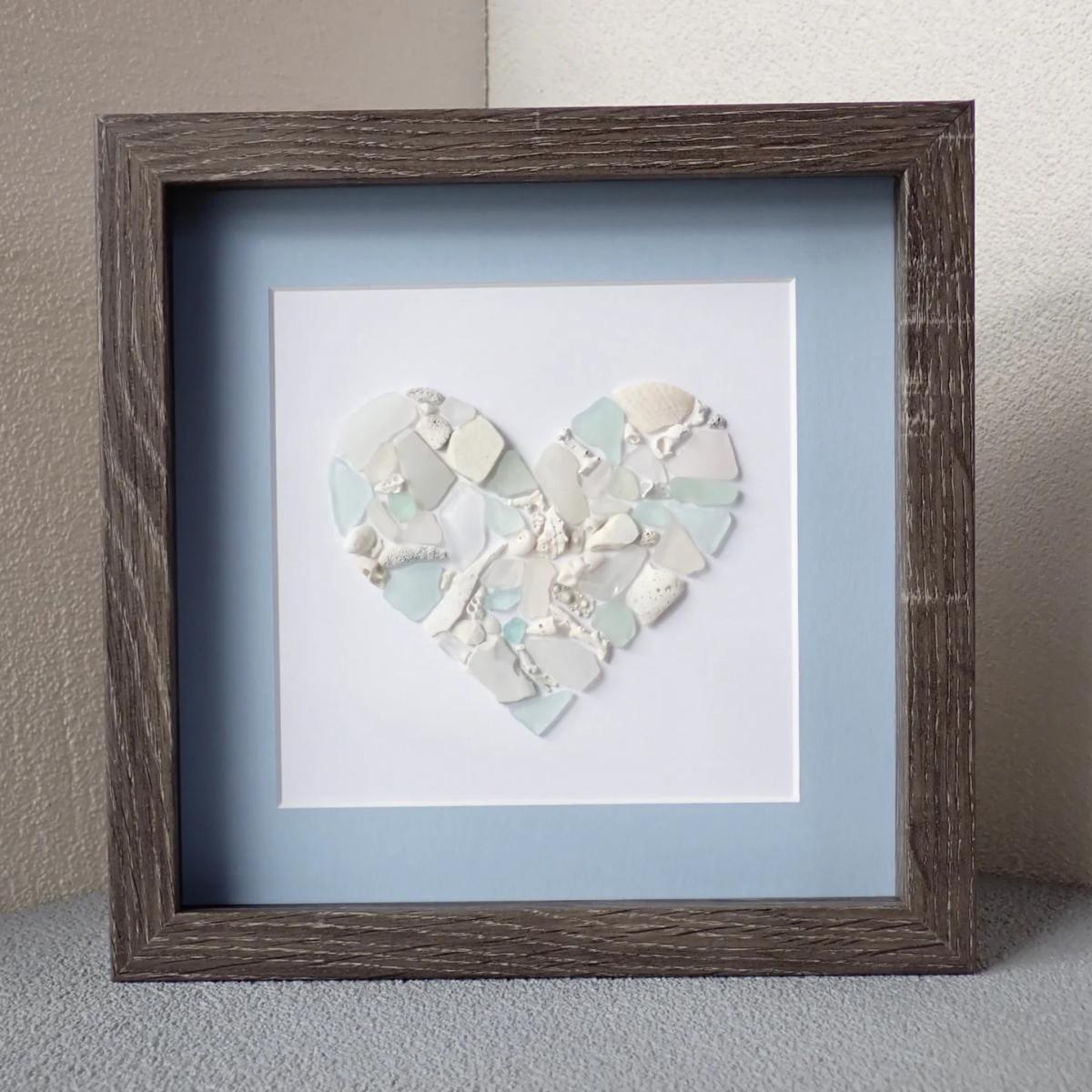 A photo of a seaglass heart framed in brown with a light blue matte.