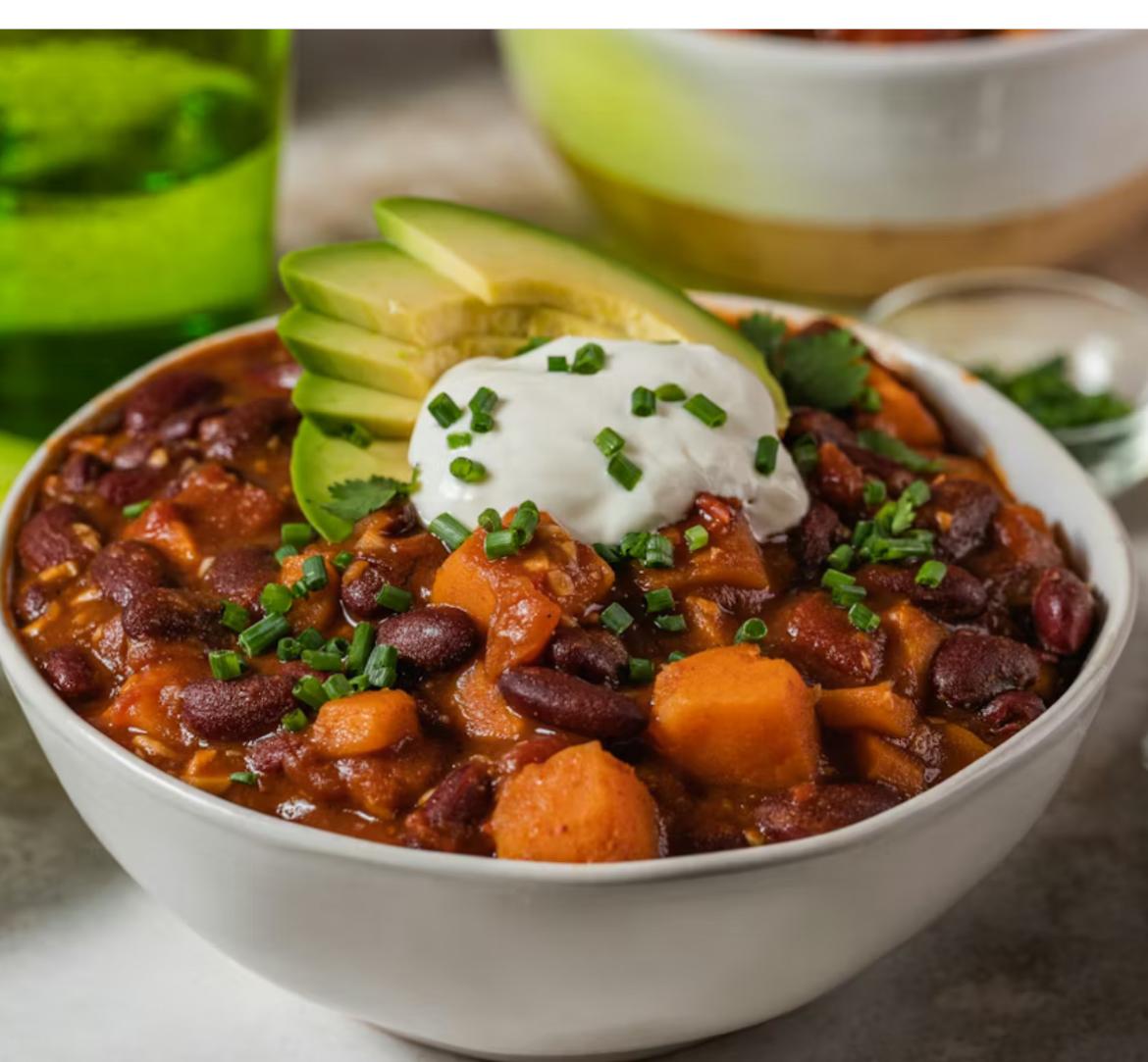 A color photo of a bowl of vegetarian chili topped with avocado slices and sour cream.